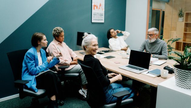 Frauen und Männder in einem Büro sitzen an einem Konferenzwisch.